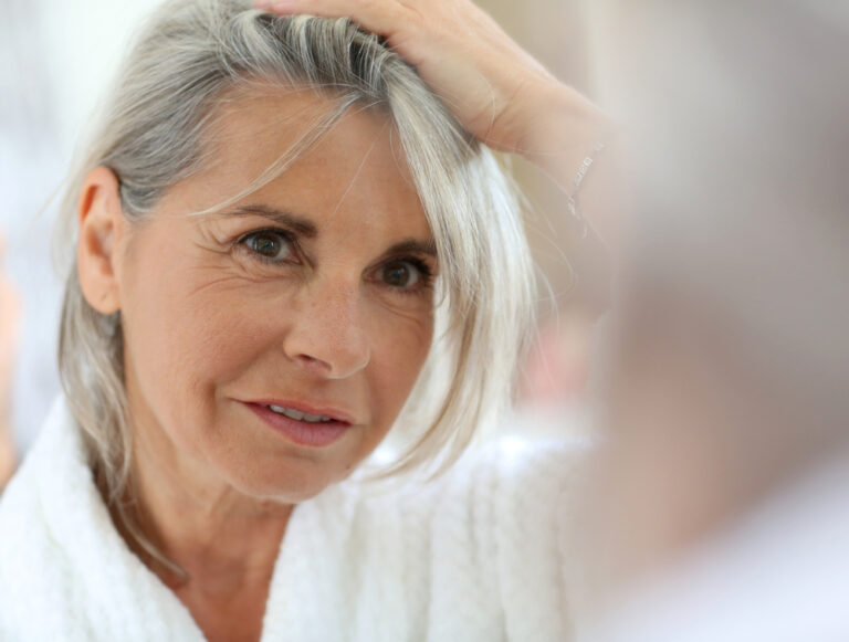Donna con capelli grigi si guarda allo specchio