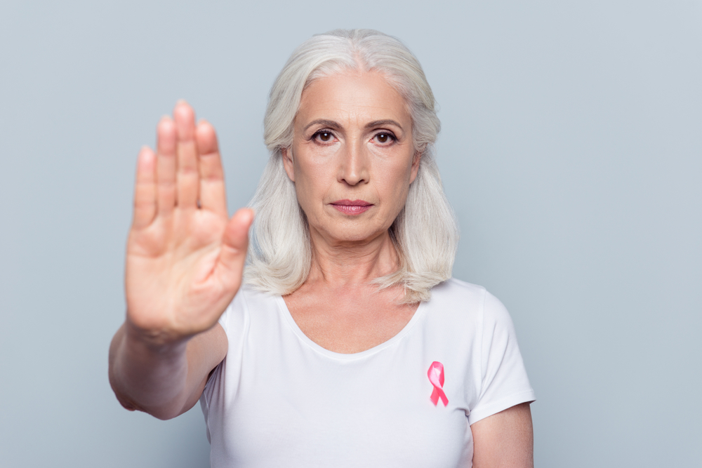 Donna con nastro rosa per tumore al seno con mano alzata in segno di stop