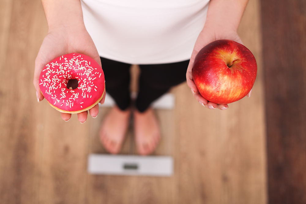 Donna su bilancia con ciambella e mela in mano: esempio di tornare in forma